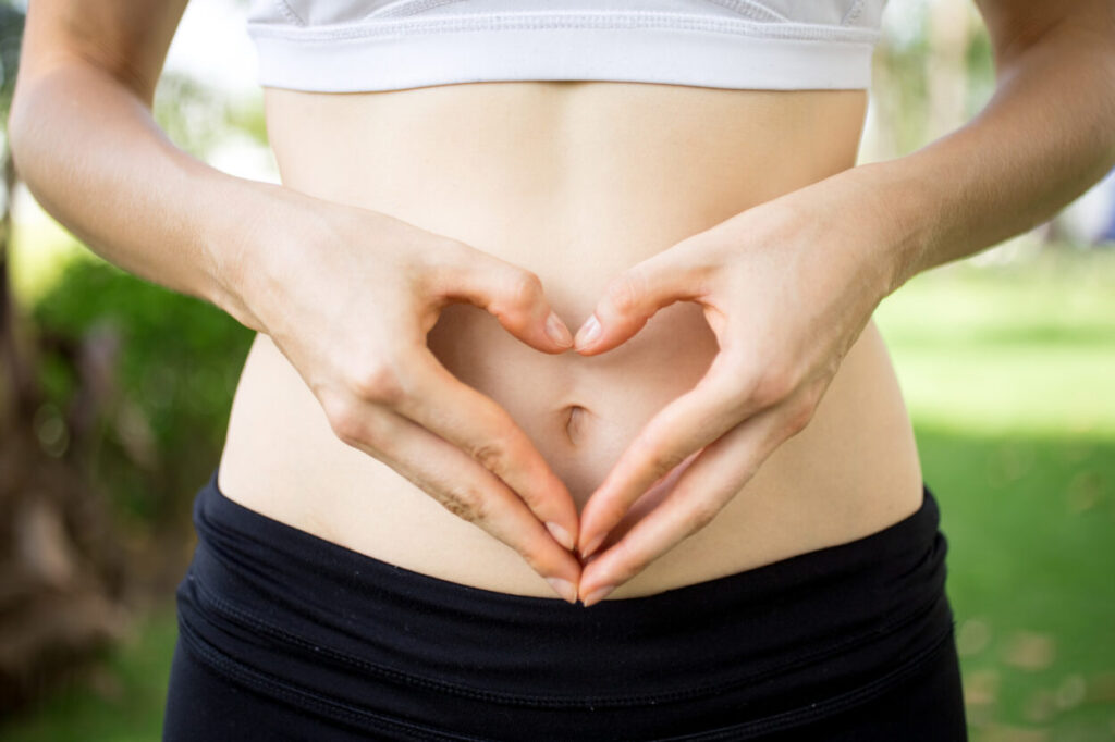 Frau formt mit den Händen ein Herz auf dem Bauch â€“ Symbol für Darmsanierung in Berlin