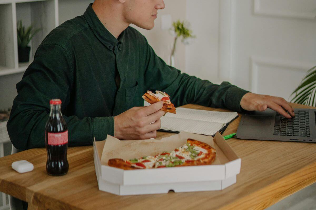 Junger Mann isst Pizza am Computer mit Cola als Beispiel für hektisches Essen